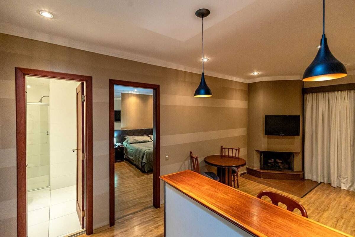 A hotel room with a wooden desk, two chairs, a TV, and a bed in the background.