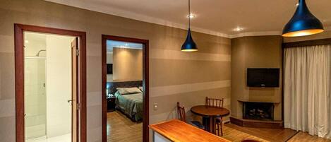 A hotel room with a wooden desk, two chairs, a TV, and a bed in the background.