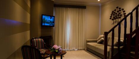 A living room with a sofa, a television, a coffee table with flowers, and a staircase.