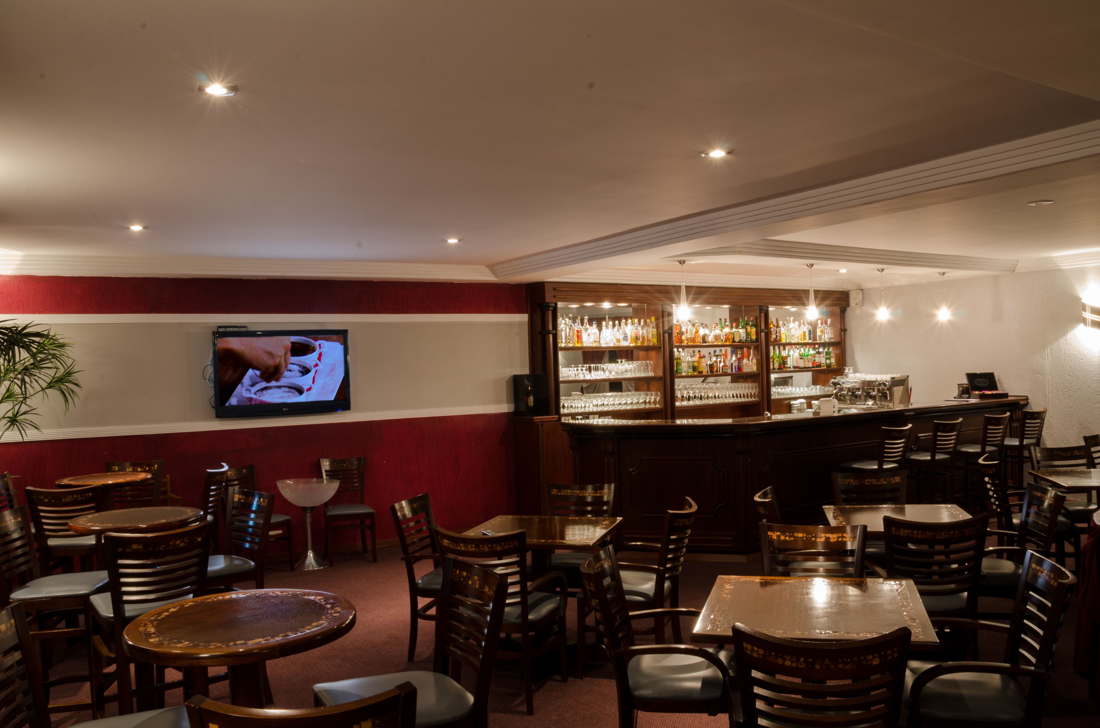 A bar area with wooden tables and chairs, a television mounted on the wall, and a well-stocked bar counter.