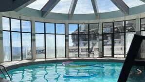 An indoor swimming pool with clear glass walls, a tiled floor, and a view of buildings outside. - Home Green Home (Campos do Jordão)