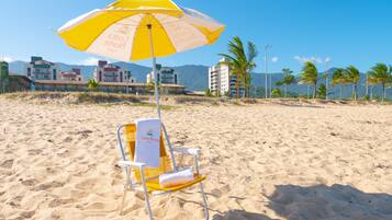 A beach chair with a towel and a yellow and white umbrella, set against a backdrop of buildings and palm trees.