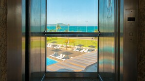 An elevator with a view of a poolside area and a beach.