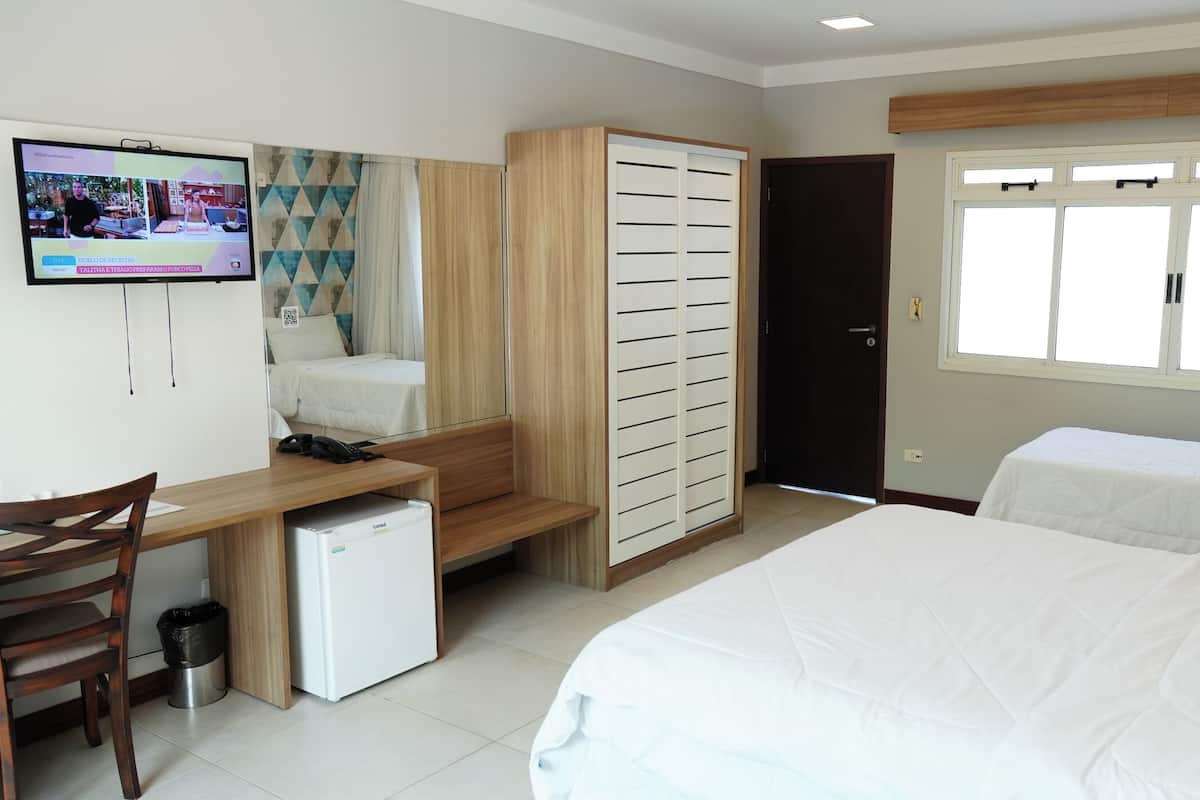 A hotel room with a bed, a desk, a small fridge, a wardrobe, and a TV.