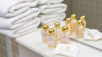 Neatly stacked white towels and bottles of Costa Norte Hotel shampoo and conditioner on a bathroom counter.