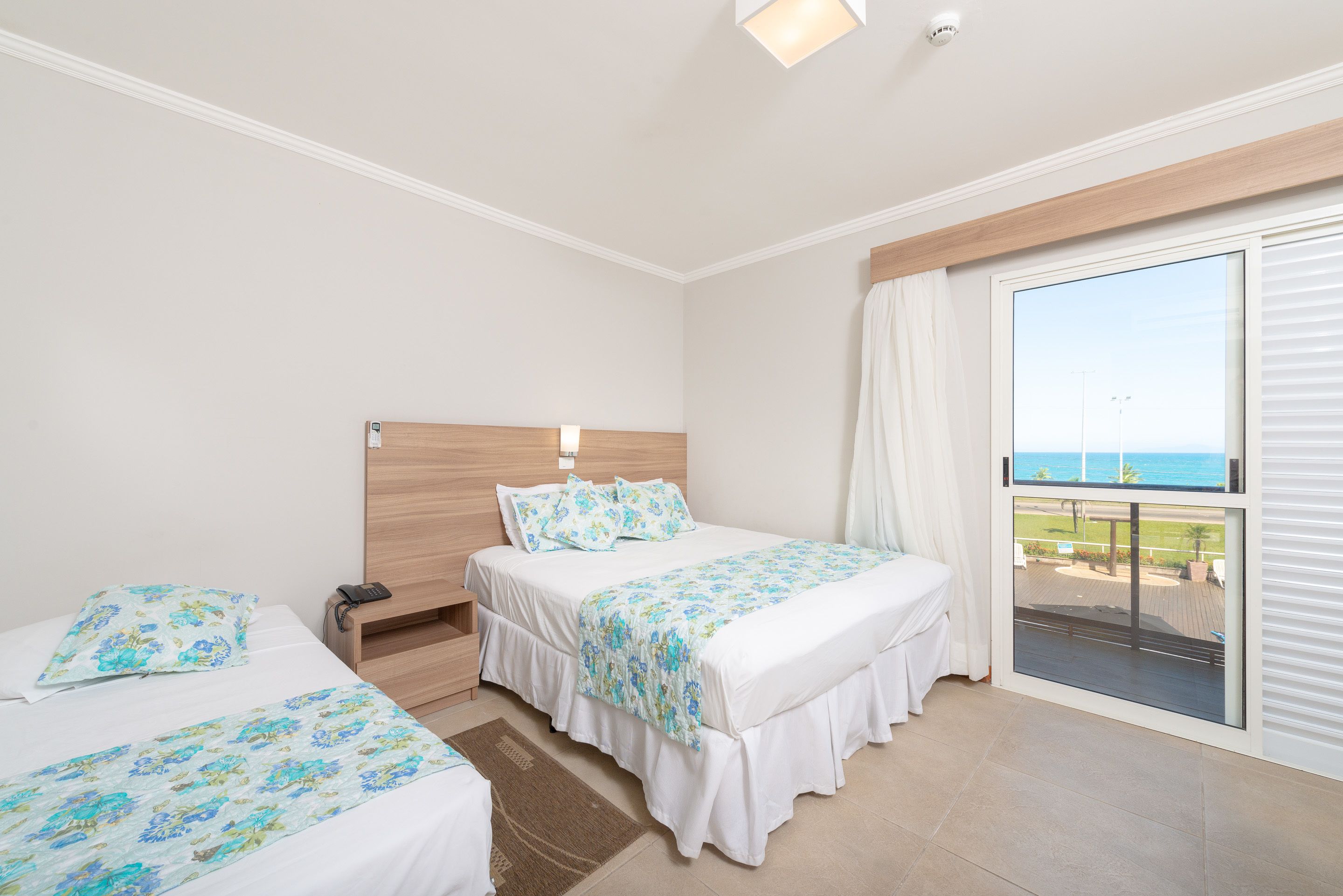 A hotel room with two beds, a balcony with a view of the sea, and a large window.