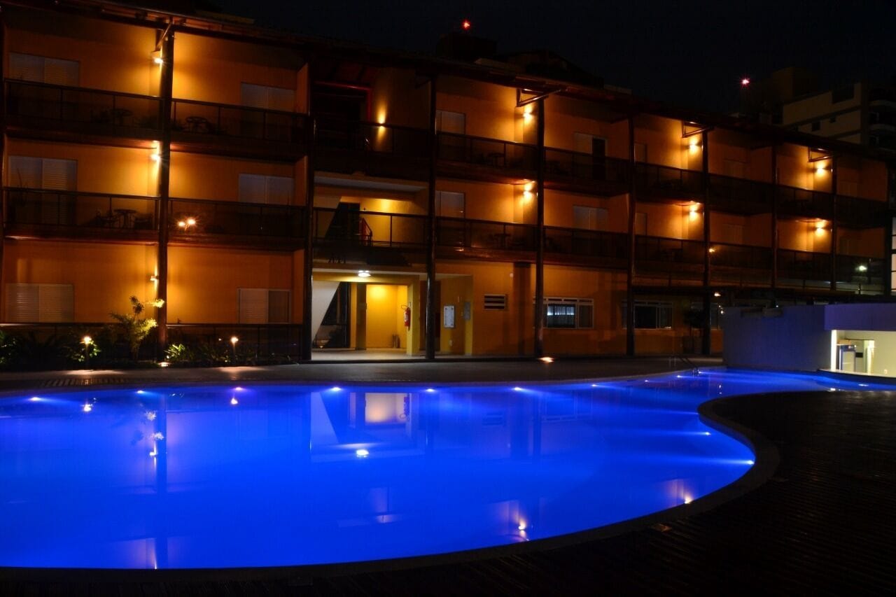 A multi-story hotel with a swimming pool at night, illuminated by blue lights.