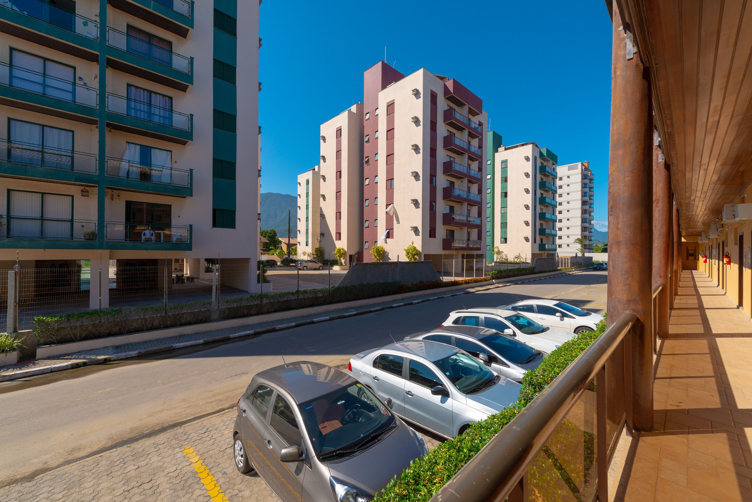 Fila de coches aparcados a lo largo de una calle con edificios altos al fondo.
