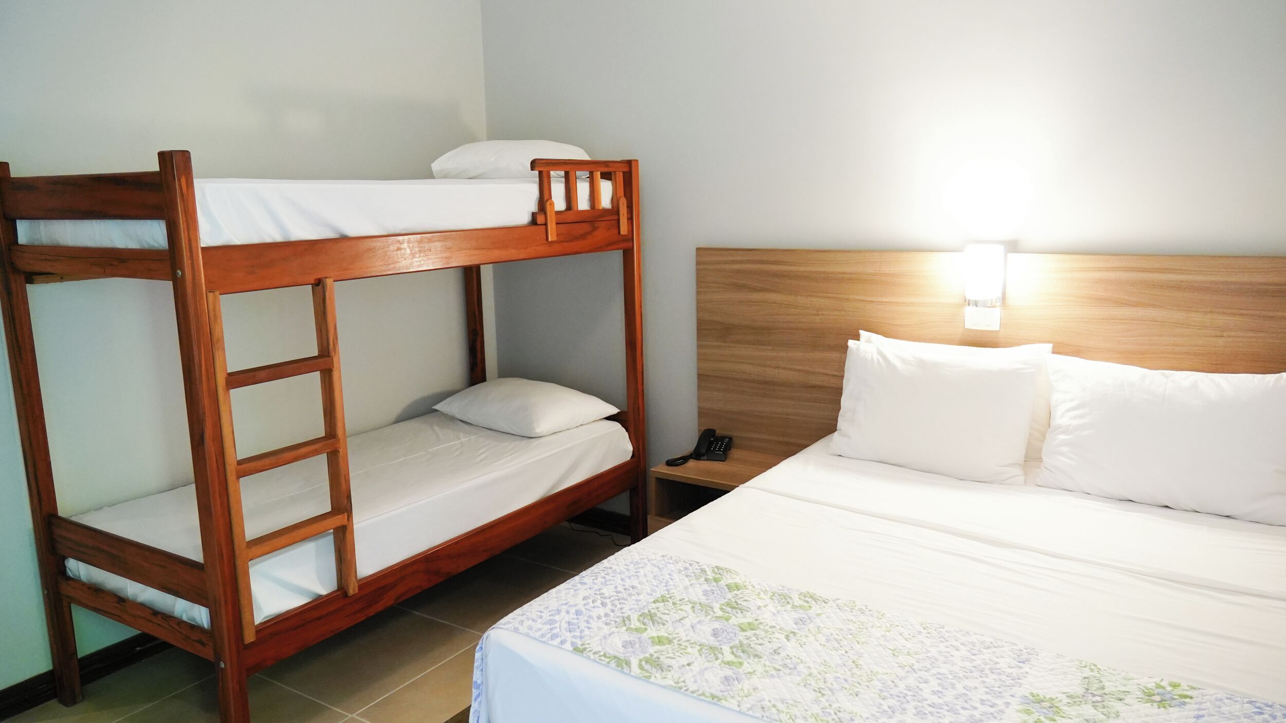 A bunk bed with a ladder, a bedside table with a phone, and a bed with a floral-patterned bedspread.