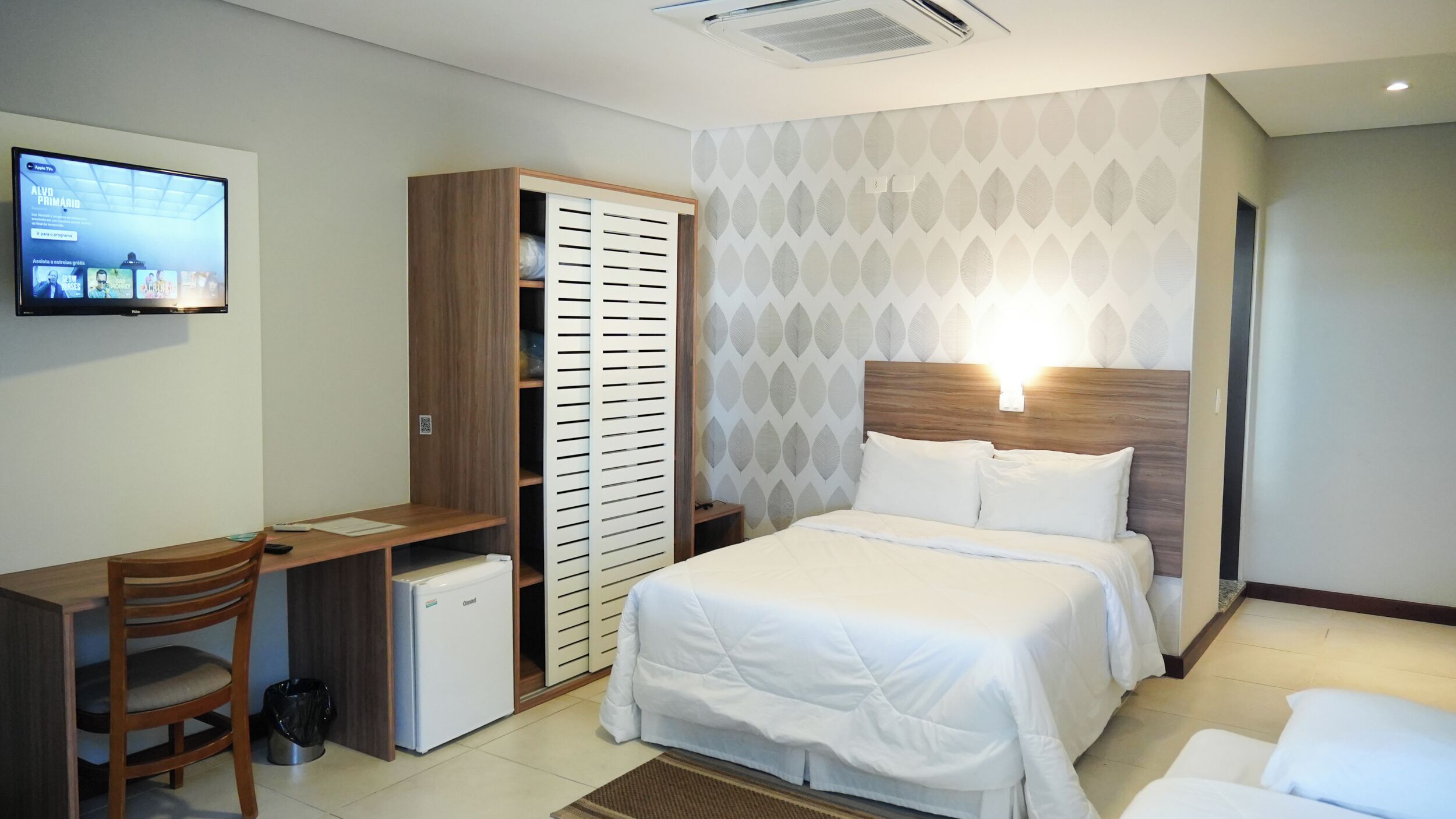 Une chambre d’hôtel équipée d’un lit, d’un bureau, d’une armoire et d’un téléviseur fixé au mur.