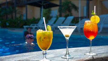 Three cocktails on a poolside table with a pool and lounge chairs in the background.