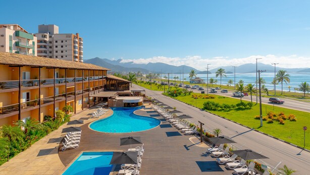Un hotel con piscina, una carretera con coches y vistas al océano y las montañas.