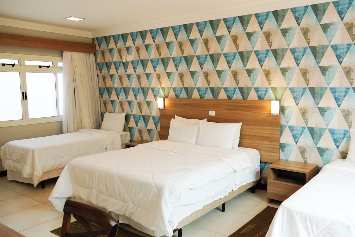 A hotel room with two single beds and a double bed, wooden headboard, and a geometric patterned wall.