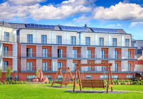Edifício residencial com vários andares, painéis solares, um pátio gramado e balanços de madeira.