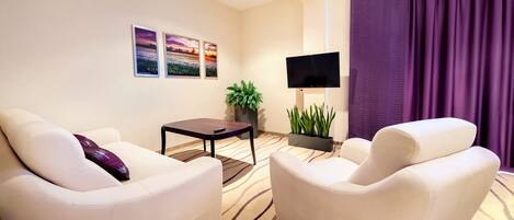 A modern living room with two white sofas, a flat-screen TV, a small table, and a potted plant.
