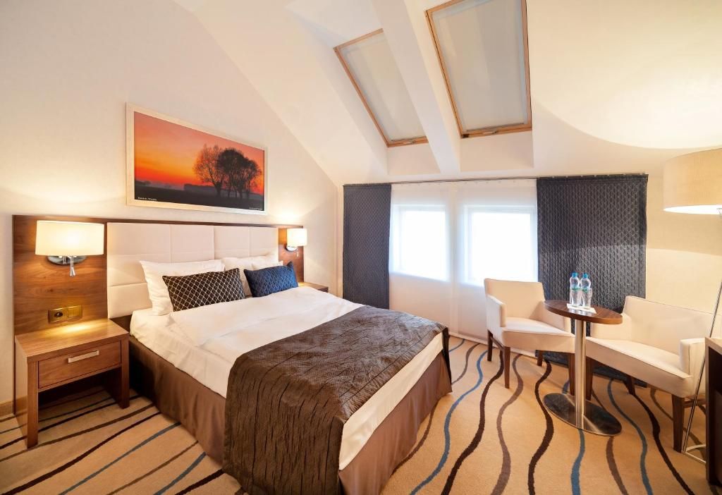 Habitación de hotel con una cama grande, un escritorio, una silla, una ventana con cortinas y un cuadro en la pared.