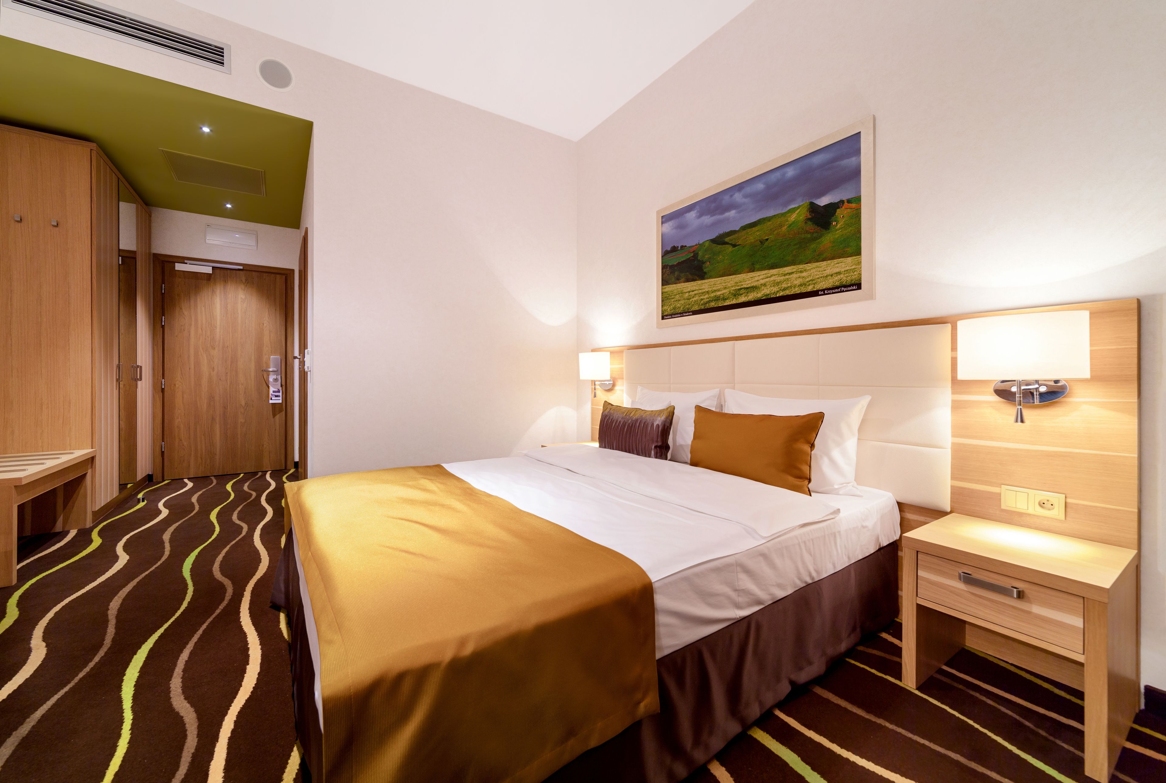 Une chambre d’hôtel avec un lit, des tables de chevet, une commode, un tableau au mur et une porte donnant accès à la salle de bain.