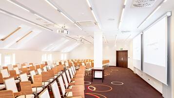 Une salle de conférence avec des rangées de chaises, un écran de projection et un grand tableau blanc.
