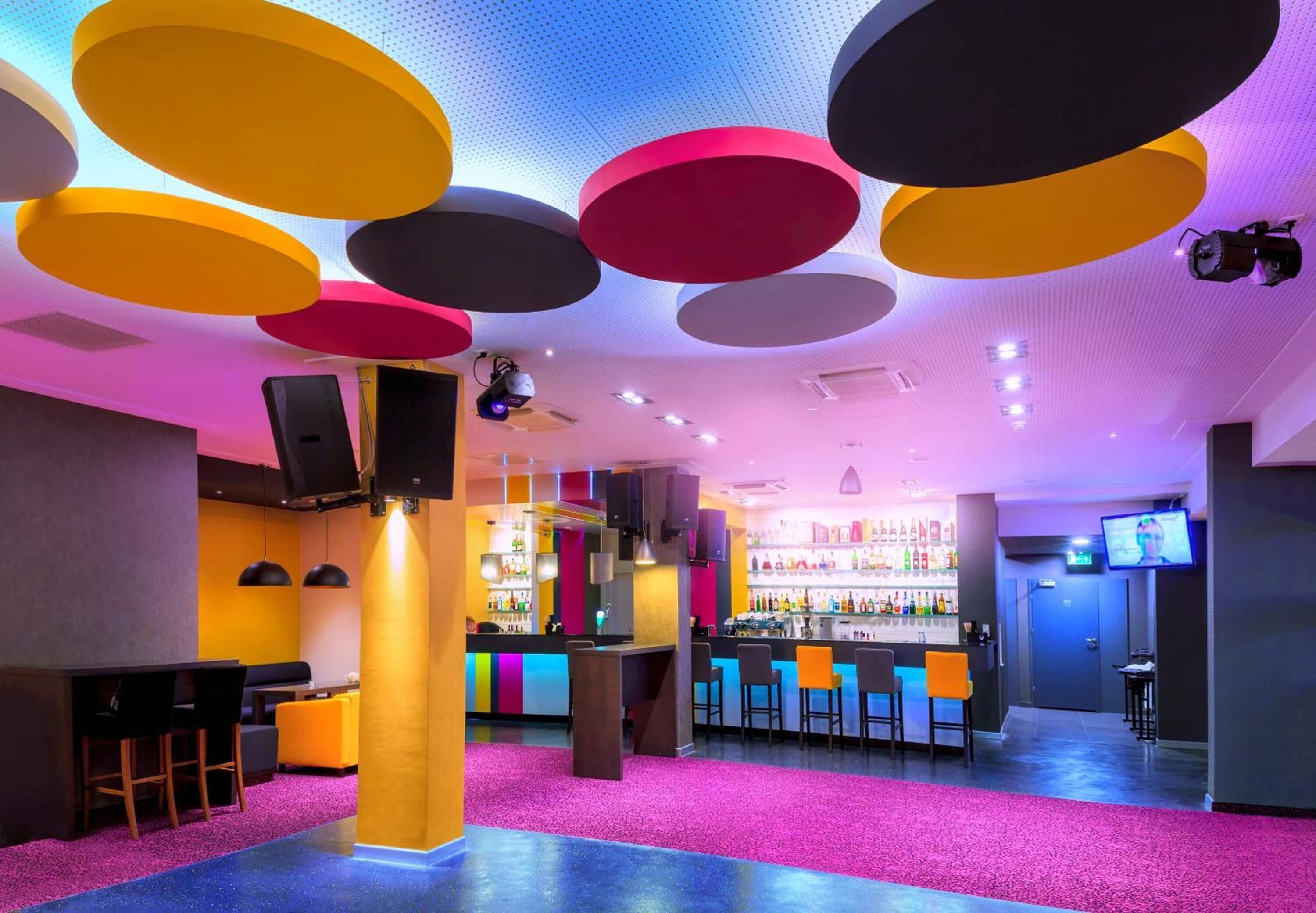 A vibrant bar area with a bar counter, seating, and a ceiling with circular light fixtures.