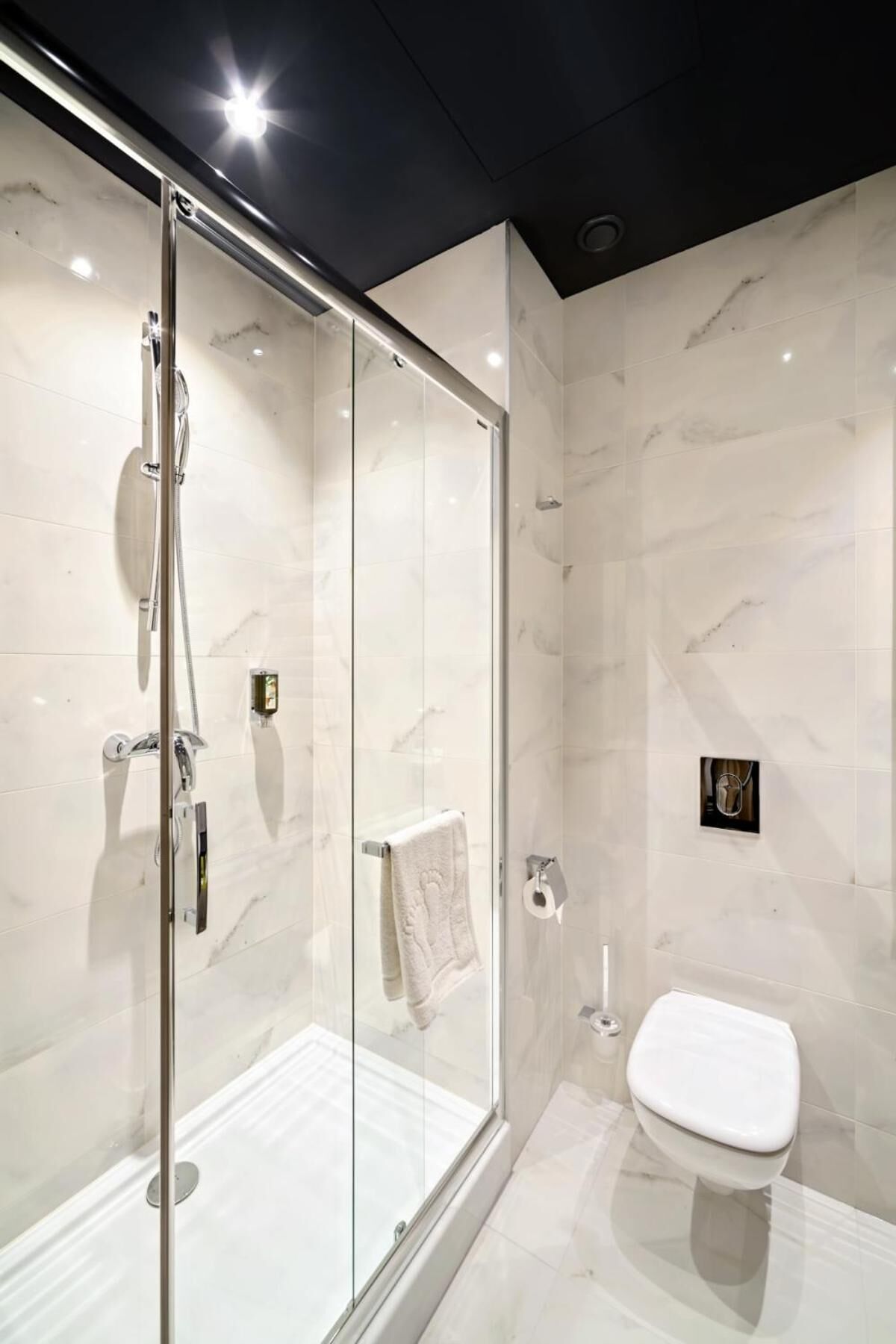 Ein modernes Badezimmer mit einer gläsernen Duschkabine, einer Toilette und Marmorwänden.