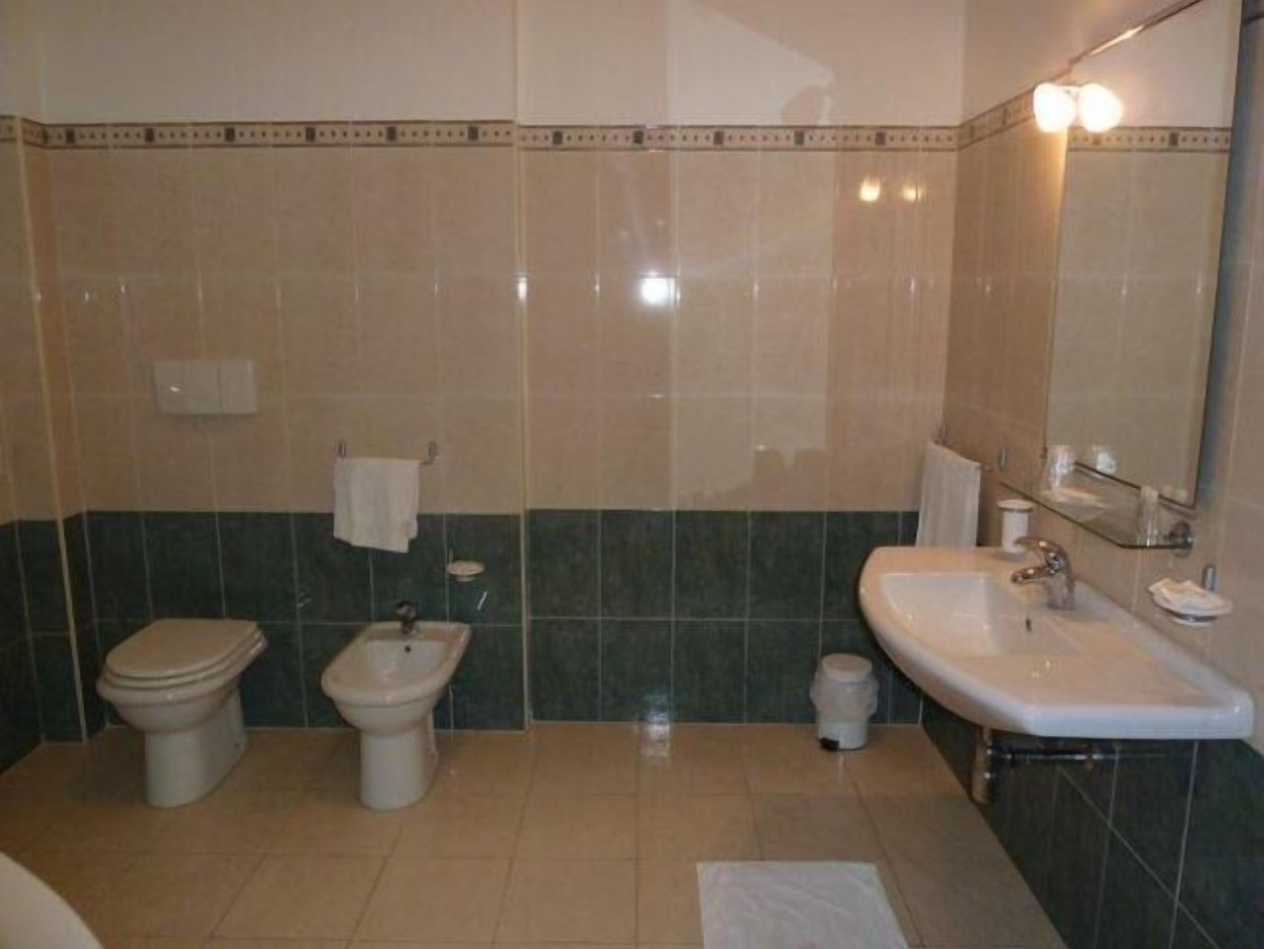 A bathroom with a toilet, bidet, sink, and mirror.