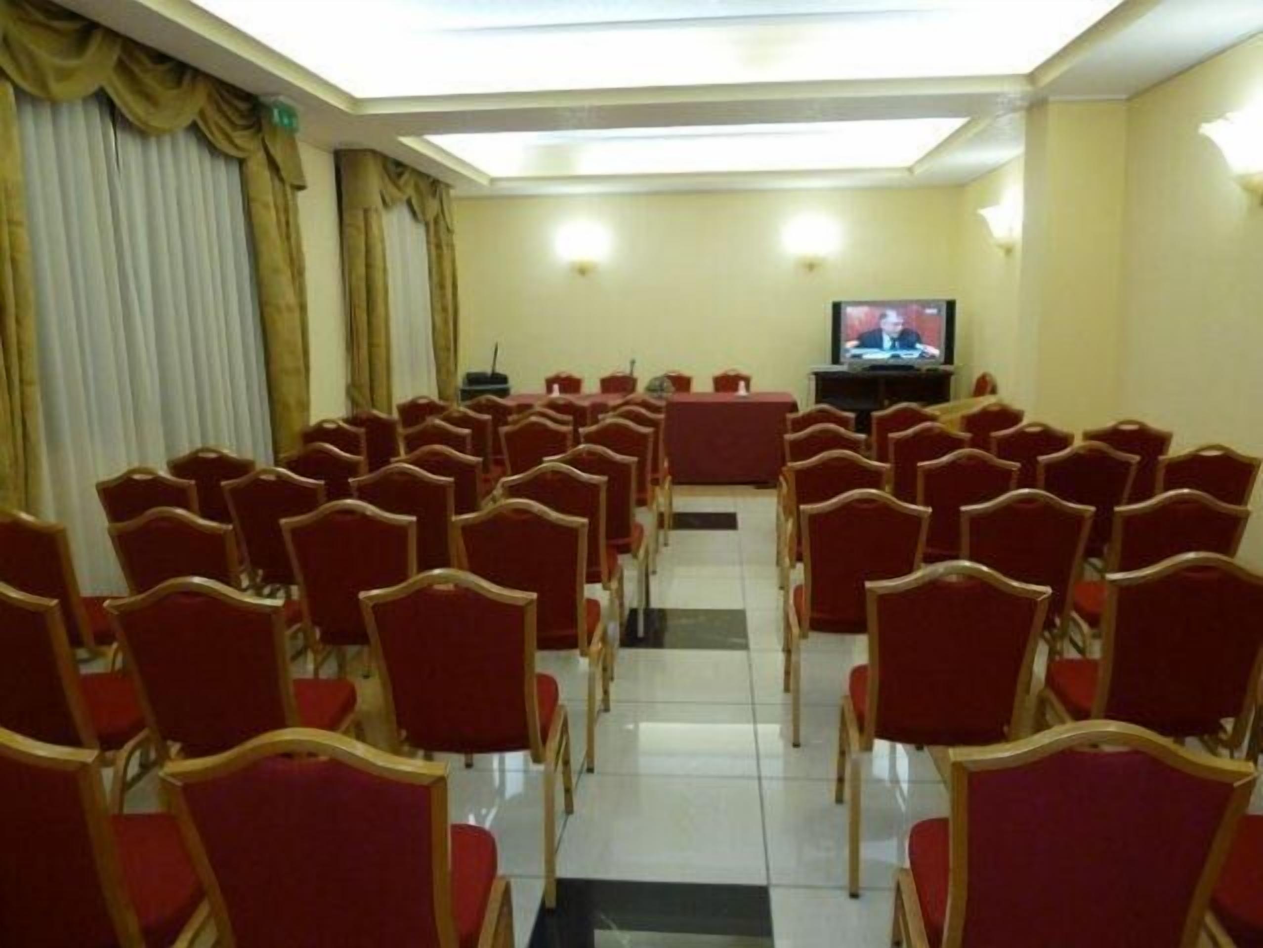 A conference room with rows of red chairs, a television screen, and a stage area.