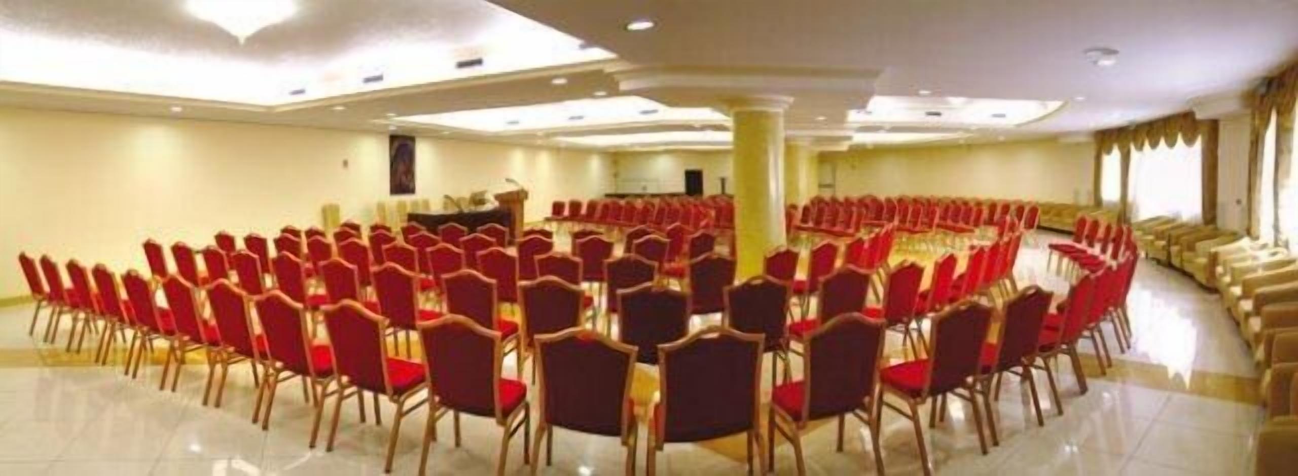A conference room with rows of red chairs arranged in a semi-circle, a podium, and a large pillar.