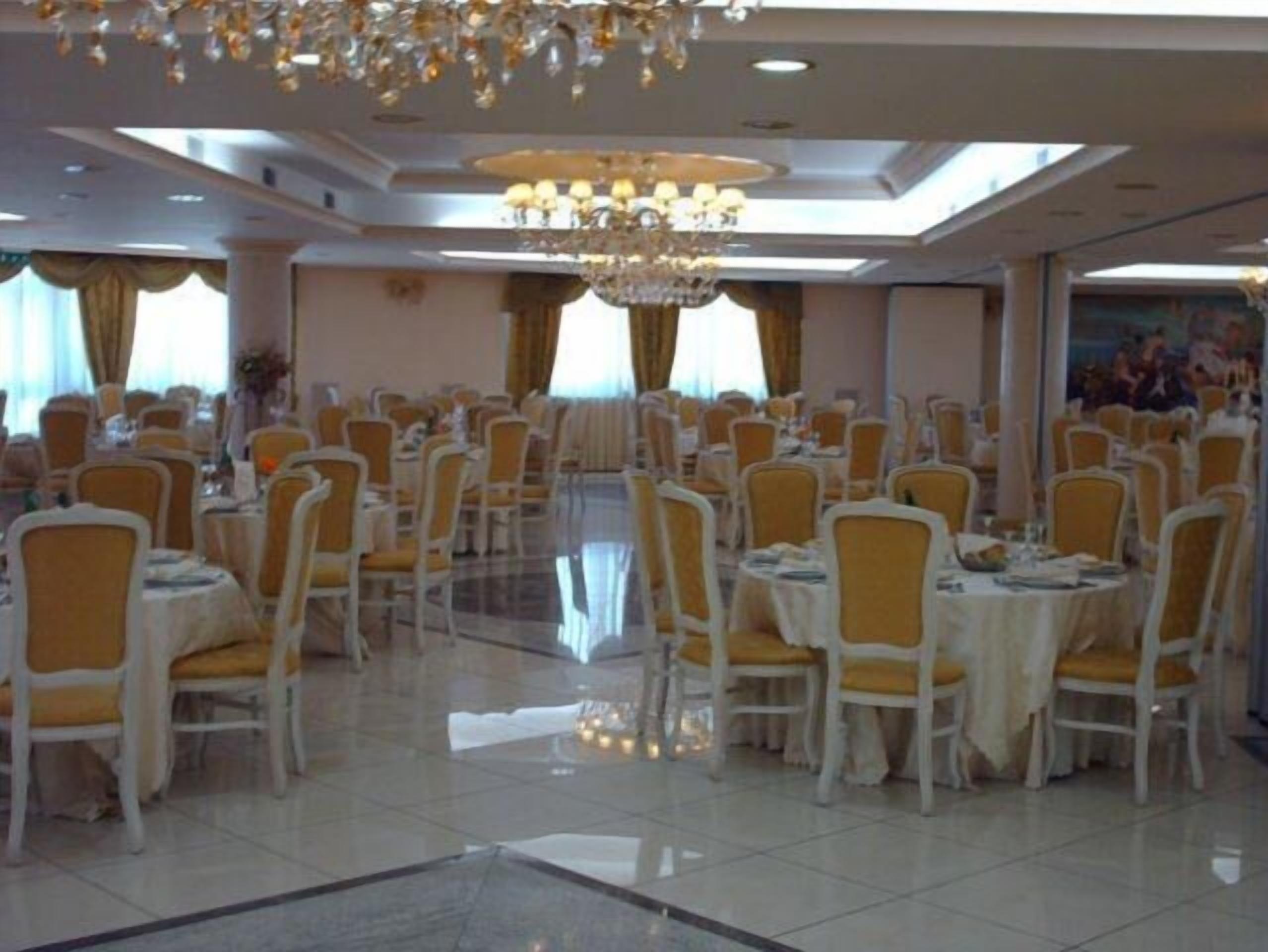 A banquet hall with round tables and chairs, chandeliers, and large windows.