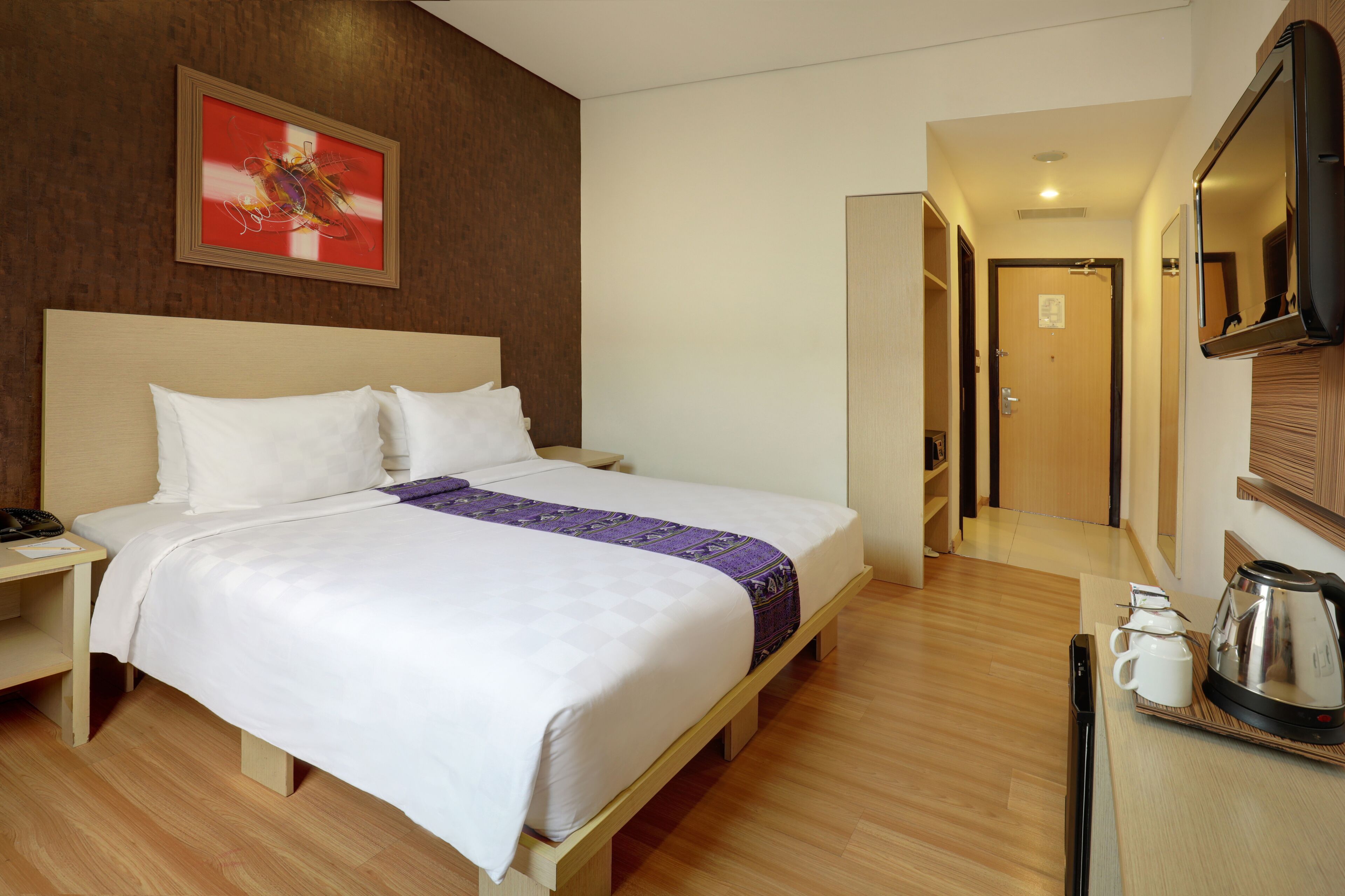 Habitación de hotel con cama, mesita de noche y cafetera en la mesita auxiliar.