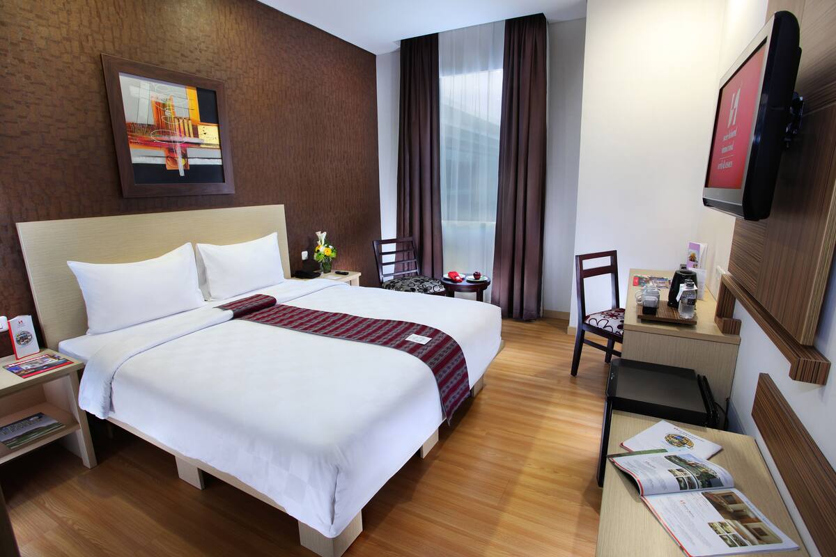 Habitación de hotel con una cama grande, un escritorio, una silla, un televisor y una ventana con cortinas.