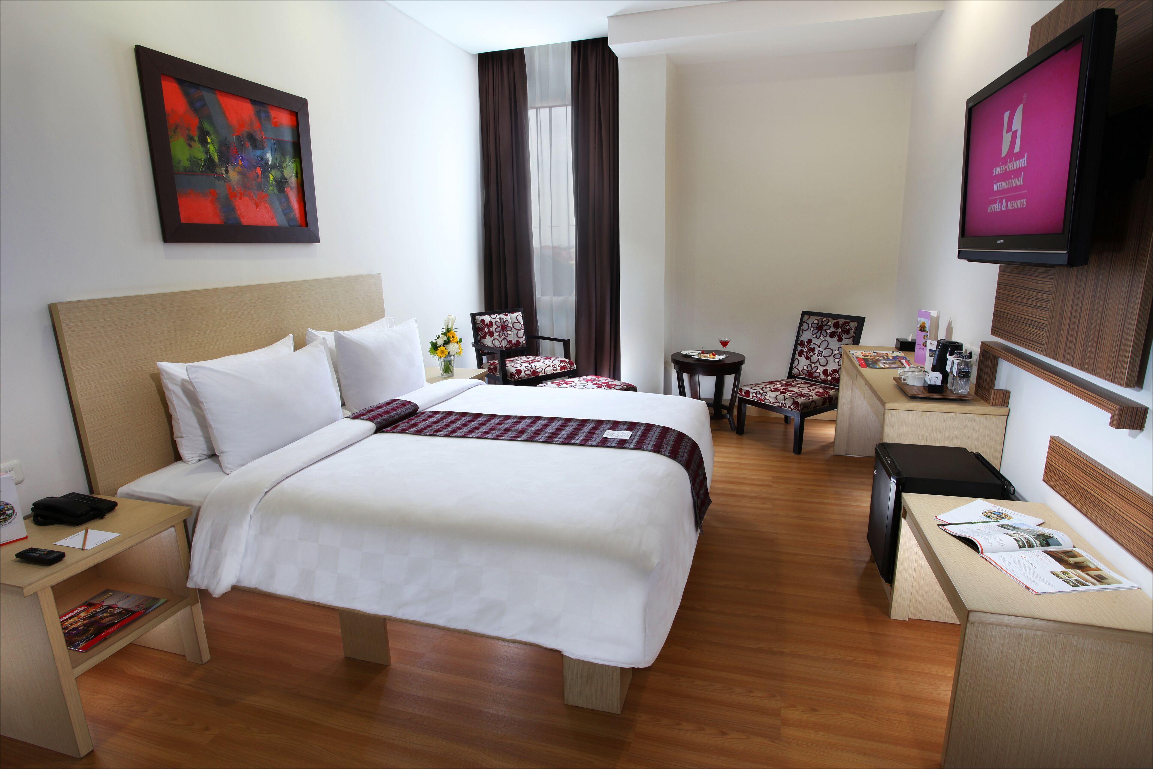 Habitación de hotel con dos camas, un escritorio, una silla, un televisor y un cuadro en la pared.