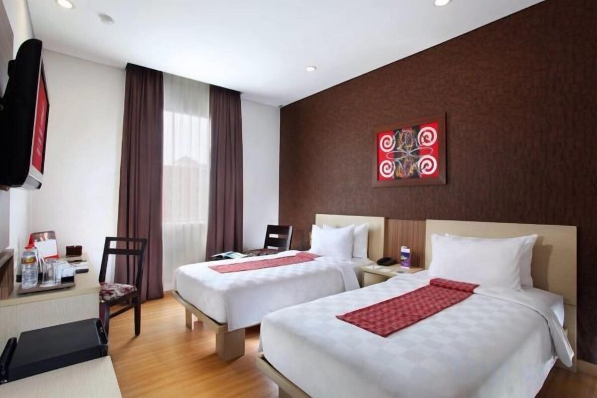 A hotel room with two beds, a desk with a chair, a TV, and a window with curtains.