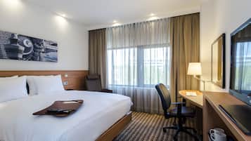 Una habitación de hotel con una cama grande, un escritorio con una silla, un televisor y una ventana con cortinas.