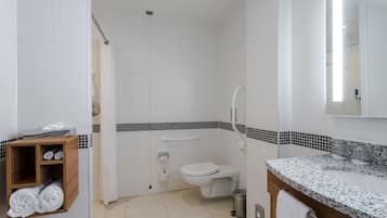 Un baño moderno con ducha, inodoro y lavamanos. Hay un perchero con toallas y un estante de madera con artículos de tocador.