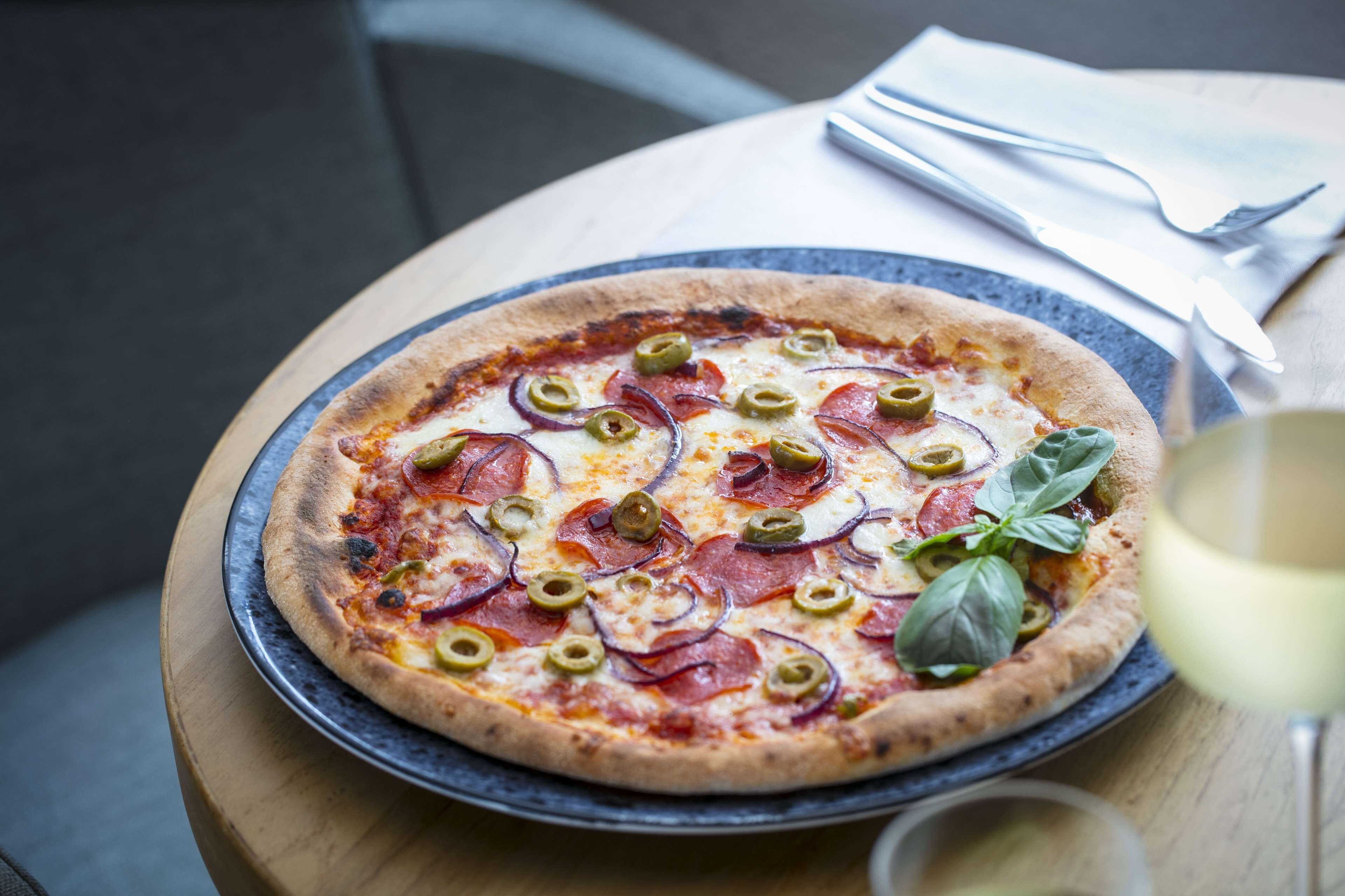 A pizza on a round table with a napkin and utensils beside it.