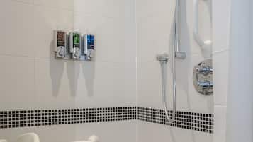 Un área de ducha con cabezal de ducha manual, grifo empotrado en la pared y otro cabezal de ducha manual. Hay tres botellas de champú y acondicionador en la pared.