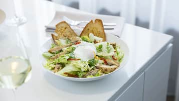 A white plate with a salad, a poached egg, and toasted bread on a white table.