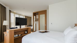 Una habitación de hotel con una cama grande, un escritorio con televisión de pantalla plana, un armario y una zona de estar con lámpara.