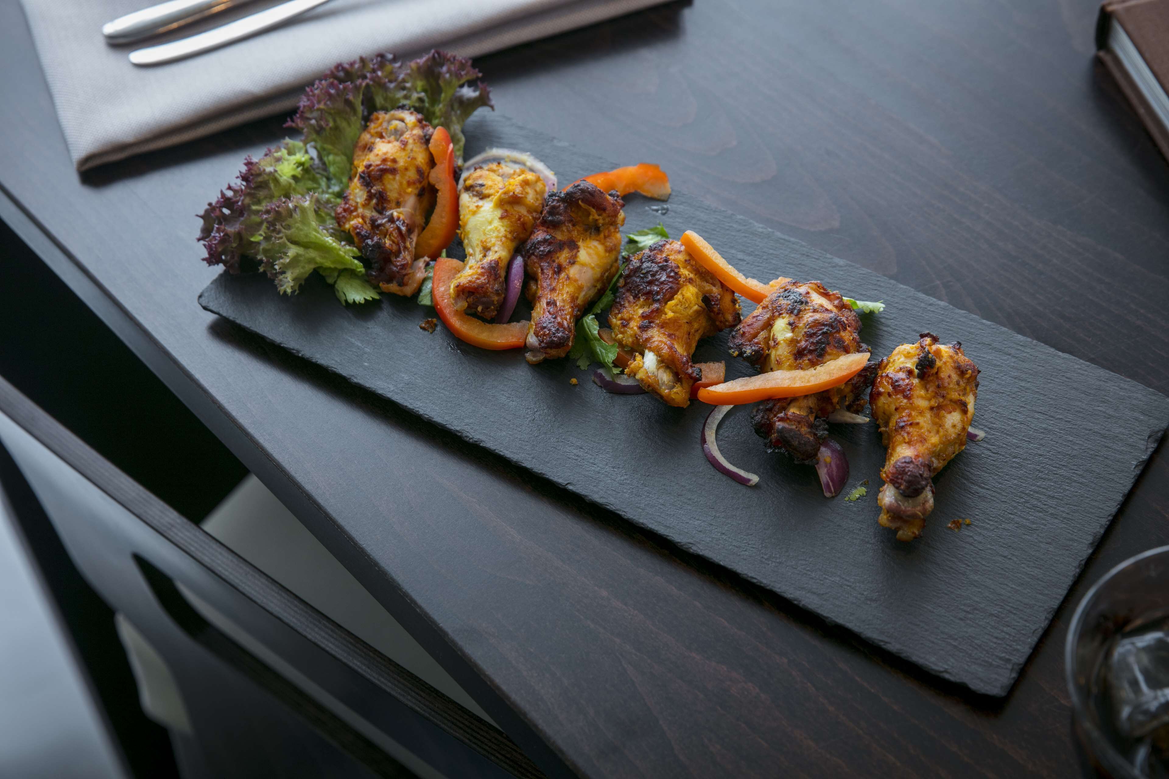 En mörk skifferbricka med grillade kycklingvingar, rödlök och skivor av morot, garnerad med sallad och örter.