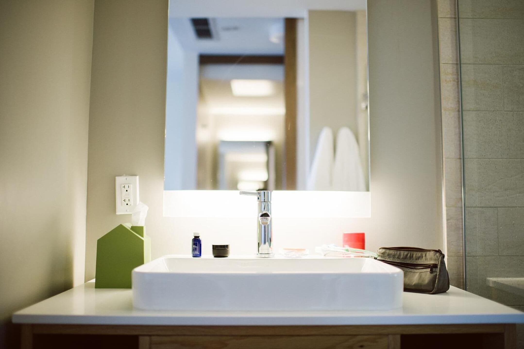 A bathroom with a white sink, a mirror, and a green soap dispenser.