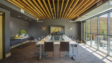 A conference room with a long table, chairs, a painting on the wall, and a large window.