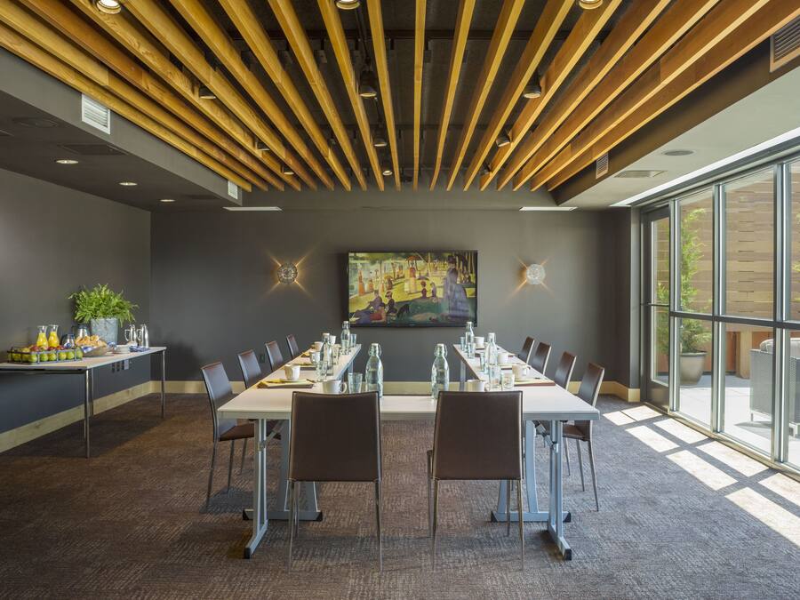 A conference room with a long table, chairs, a painting on the wall, and a large window.
