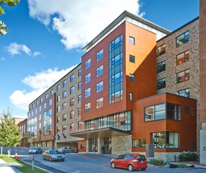 A modern multi-story hotel with a mix of brick and glass facades, large windows, and a parking lot with cars. - Hotel Vermont (Burlington)