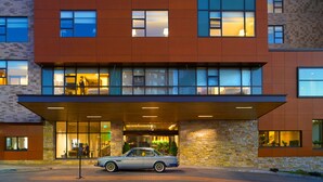 Un hotel moderno con fachada de piedra, ventanas amplias y un área de entrada cubierta.