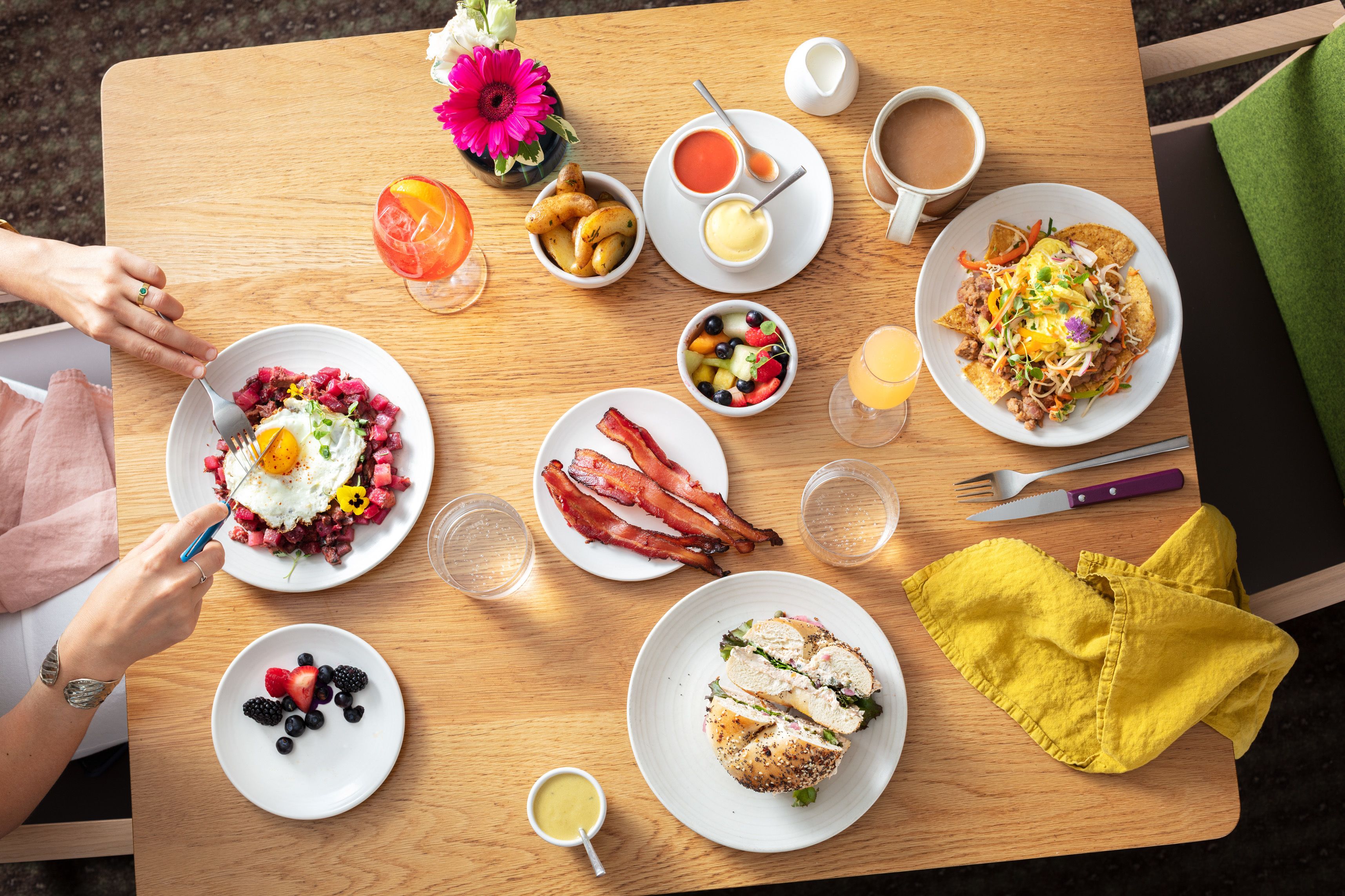 A breakfast table with various dishes, including eggs, bacon, and a sandwich, along with drinks and condiments.