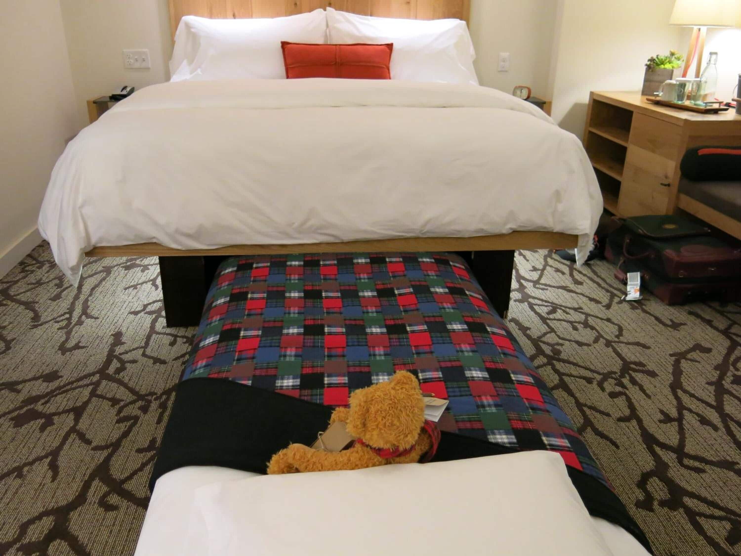 Ein Hotelzimmer mit einem großen Bett, einem Nachttisch mit Lampe, einem kleinen Schreibtisch und einem Sessel.