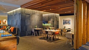 Un moderno vestíbulo de hotel con una pared de acento de piedra, techo de madera y un área de descanso con mesas y sillas.