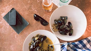 Uma mesa com mexilhões, um copo de cerveja, um smartphone e óculos de sol.