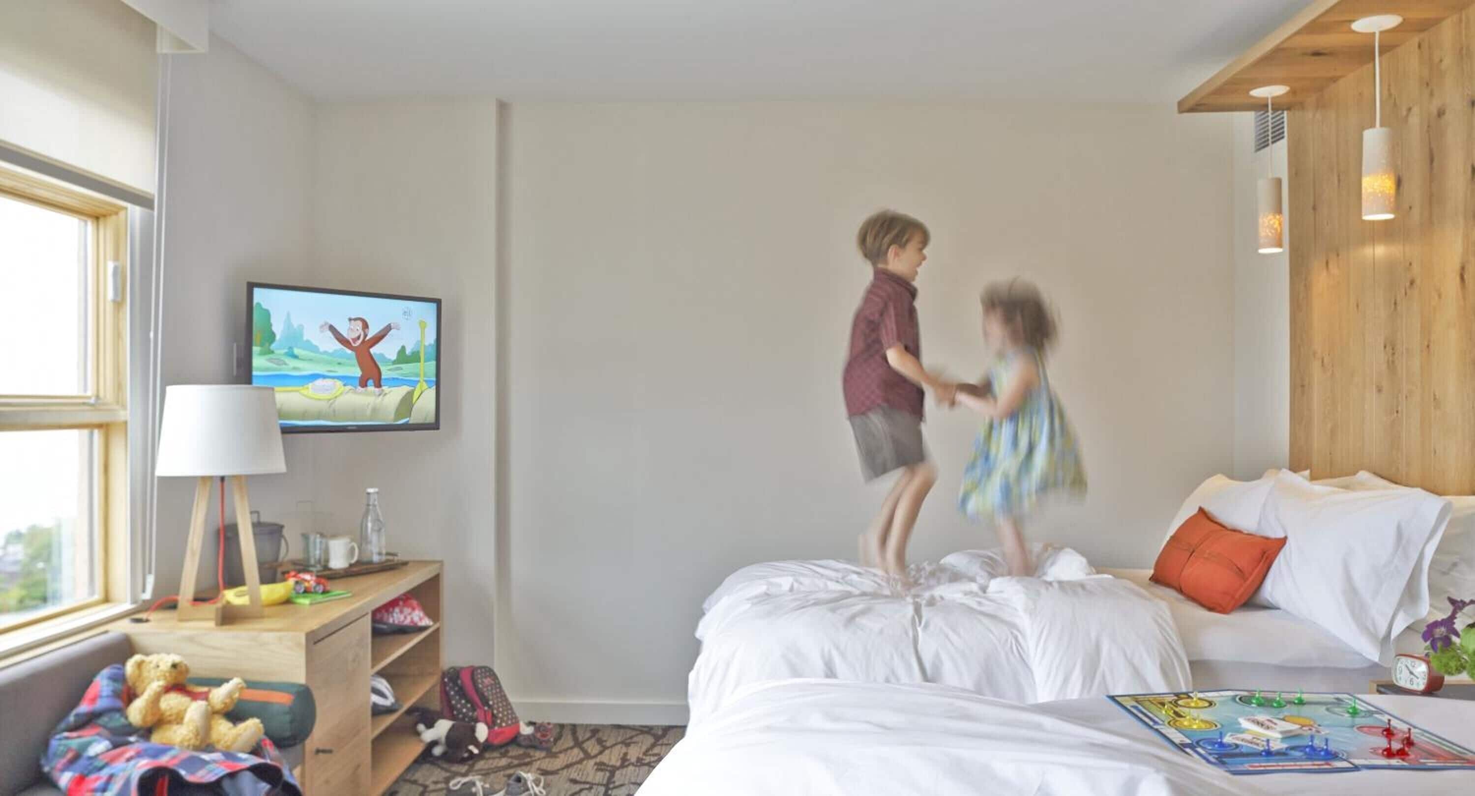 A hotel room with a bed, a television, a desk with a lamp, and a window.