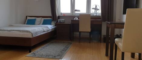 A bedroom with a bed, desk, chair, and a TV.